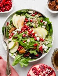 Pomegranate Salad topped with pears, pomegranate arils, pecans, and cheese, on a white background.