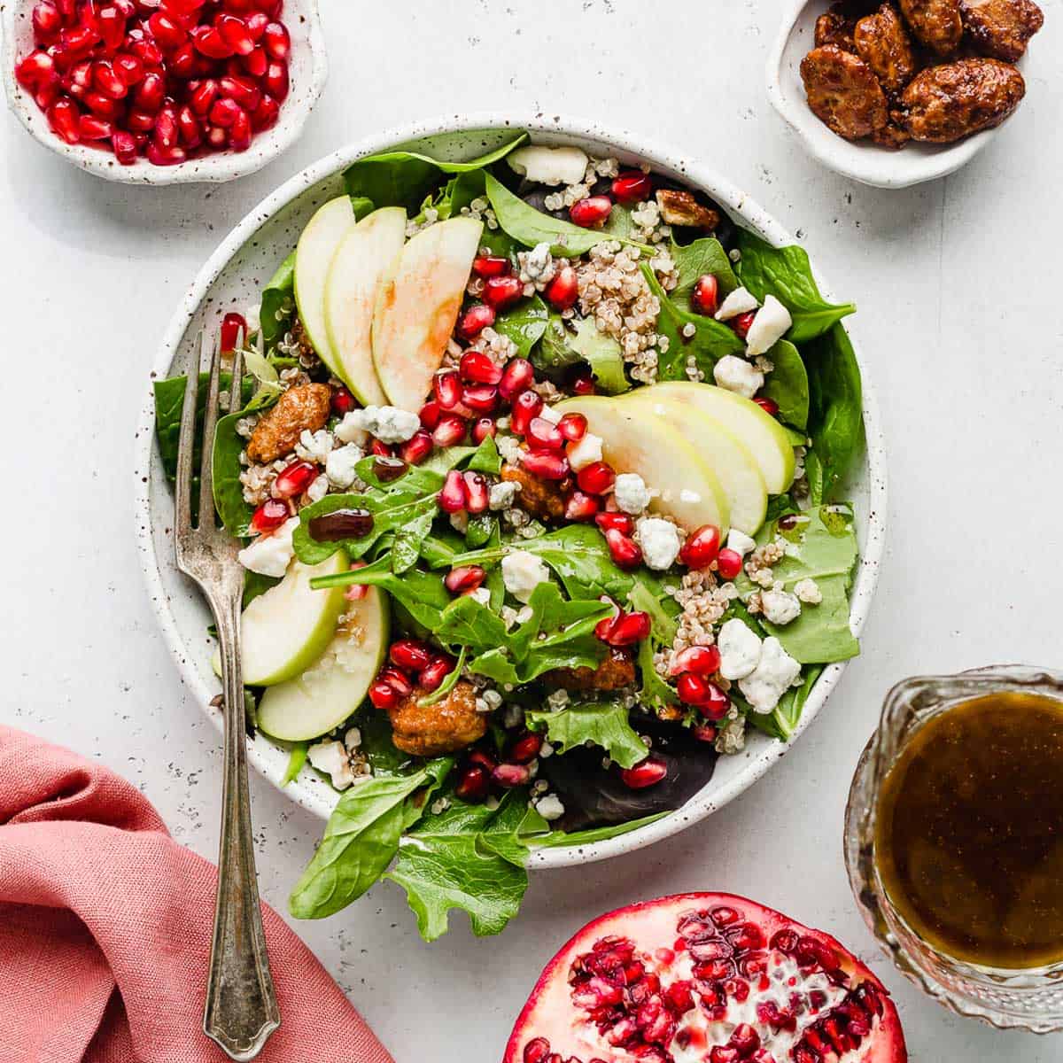 Pomegranate Salad topped with pears, pomegranate arils, pecans, and cheese, on a white background.