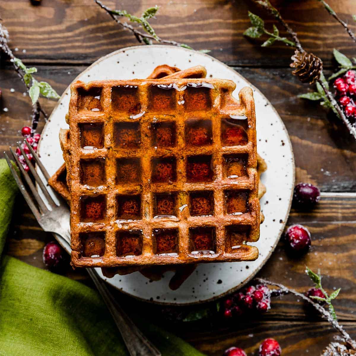 The best gingerbread waffles on a white plate covered in maple syrup.