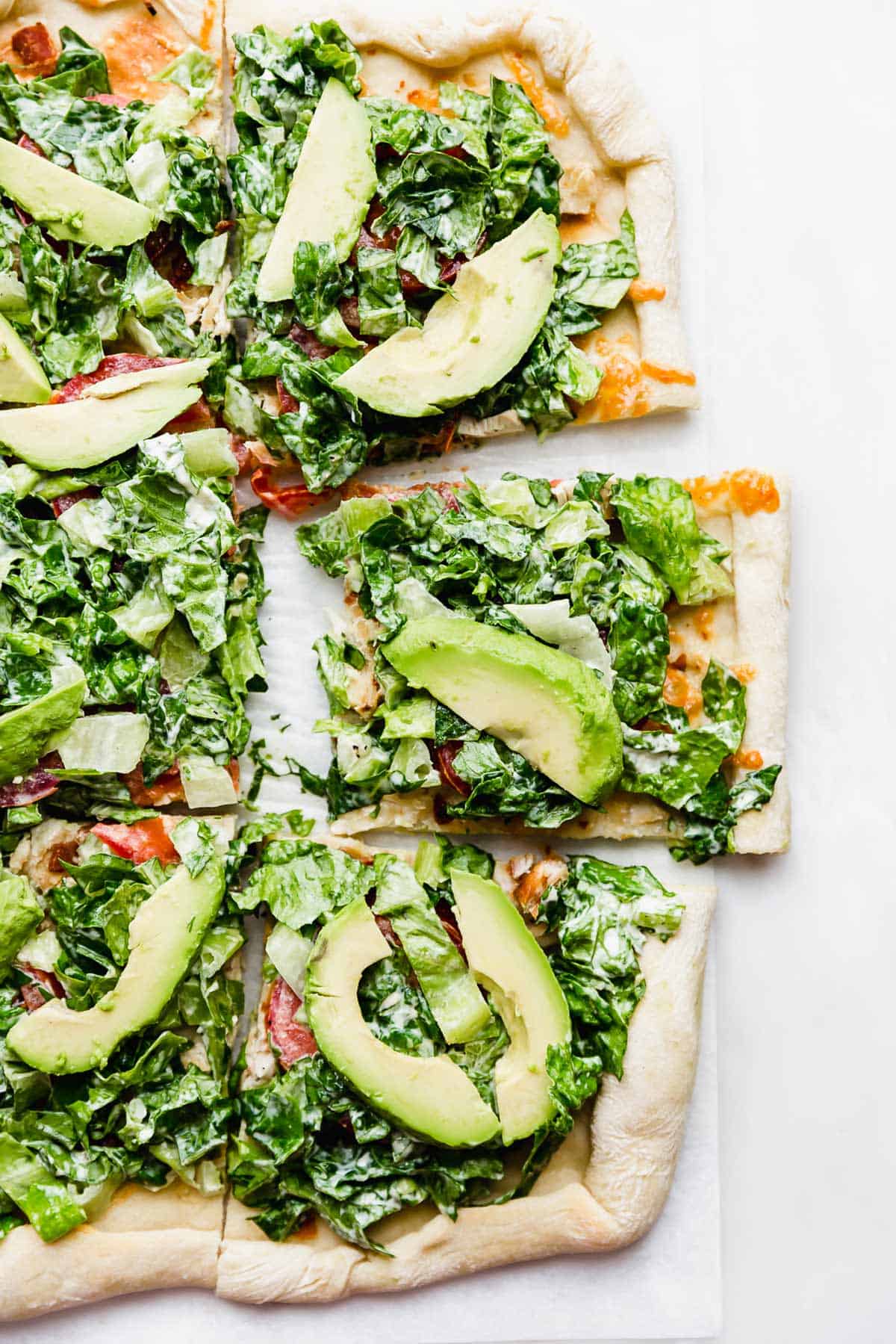 CPK Club Pizza topped with mayo covered lettuce, tomatoes, and avocado on a white background
