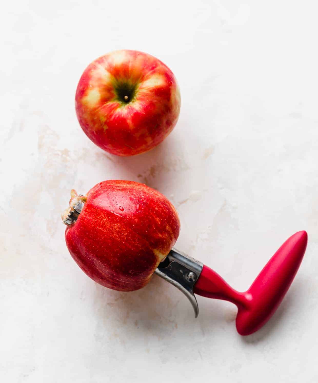 An apple corer removing the core from a red apple.