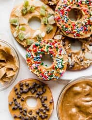 Slices of apples cut into round "donuts" topped with peanut butter, sprinkles, chocolate chips.