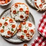 Three English muffin pizzas topped with mini pepperoni's on a gray plate.