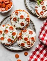 Three English muffin pizzas topped with mini pepperoni's on a gray plate.