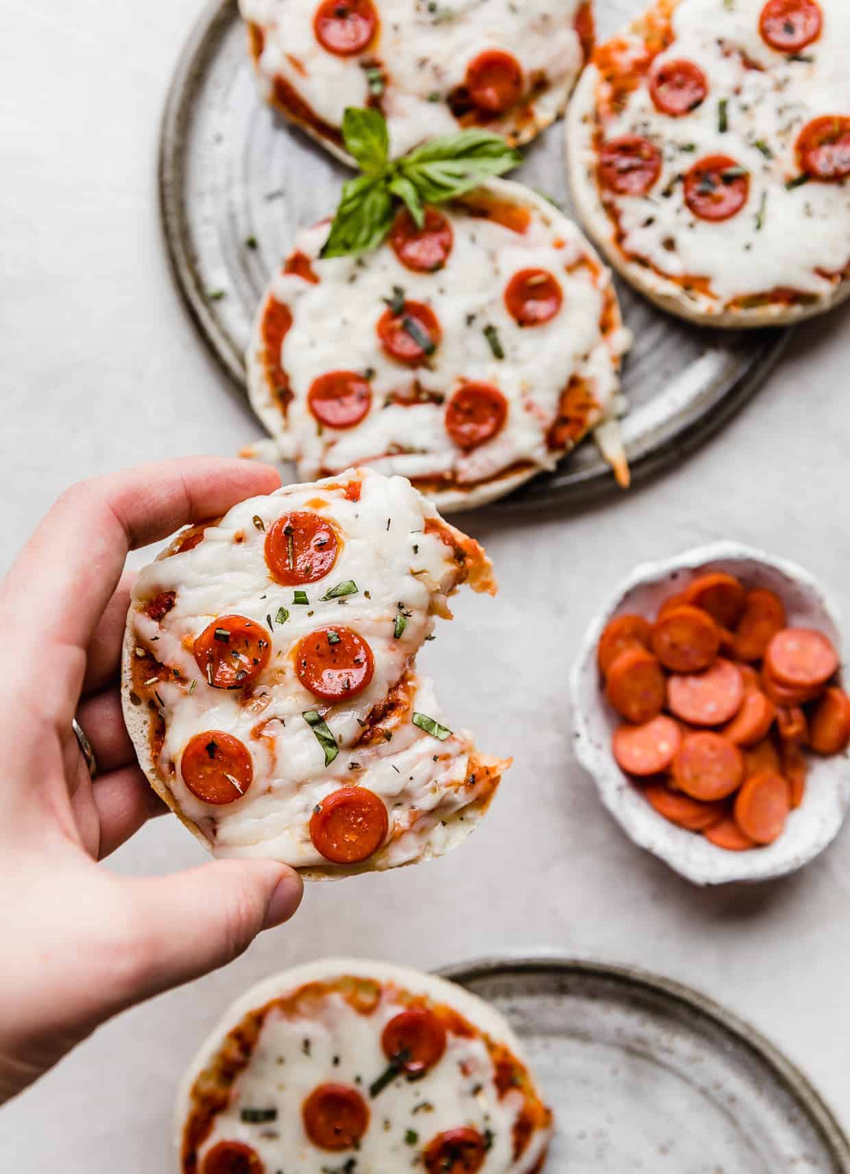A hand holding an English muffin pizzas with a bite taken out of it. 