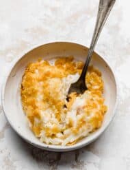 A serving of funeral potatoes on a white plate with a fork, against a white background.