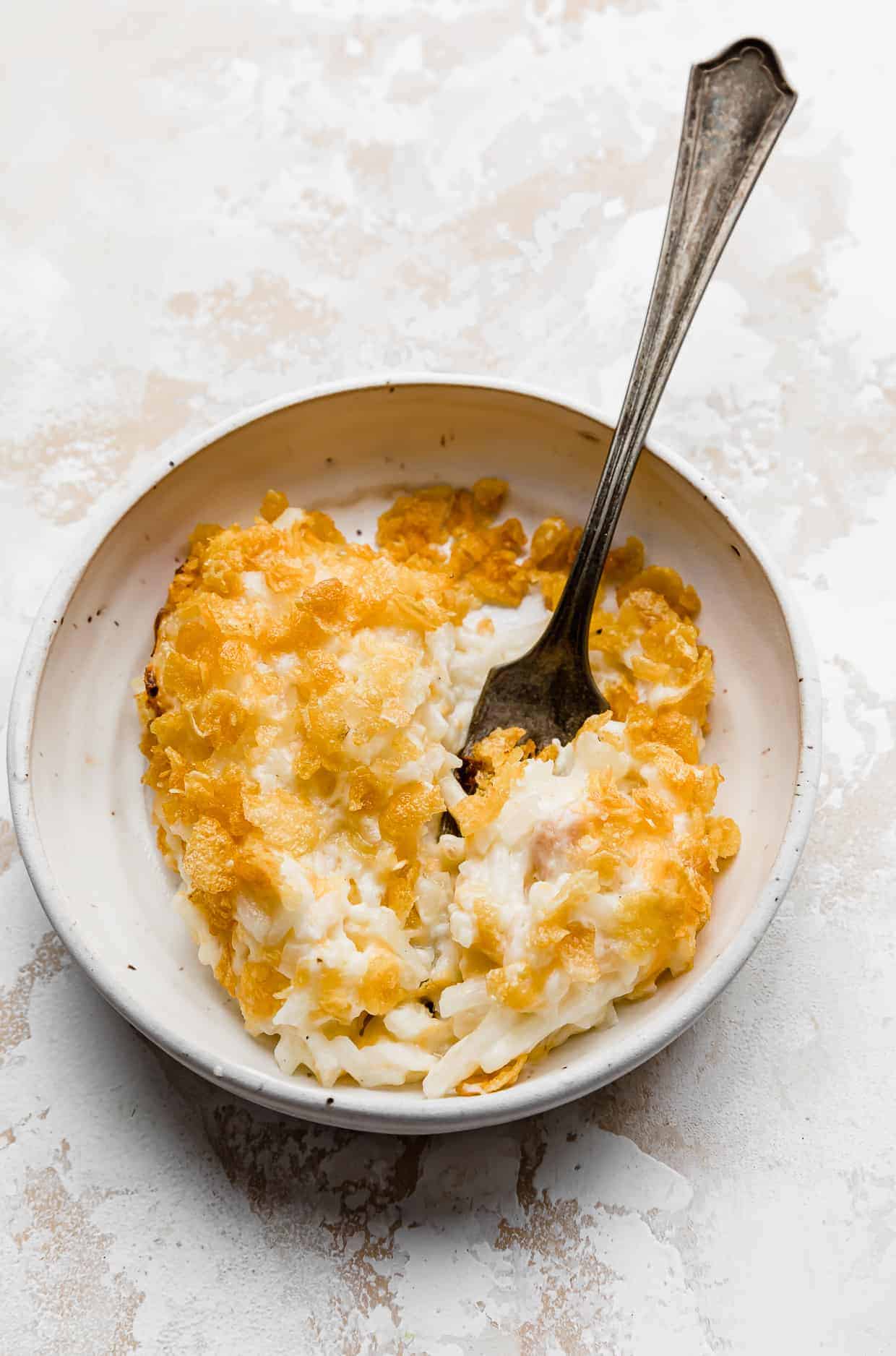 A serving of funeral potatoes on a white plate with a fork, against a white background.