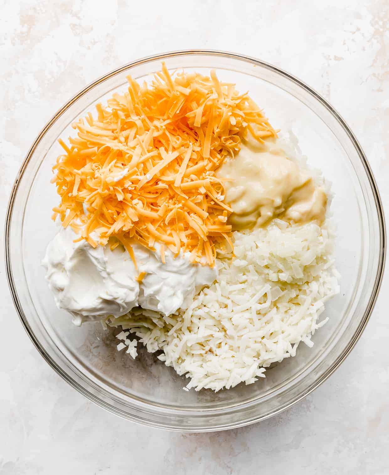 A large bowl full of shredded hashbrowns, cheddar cheese, sour cream, and cream of chicken.