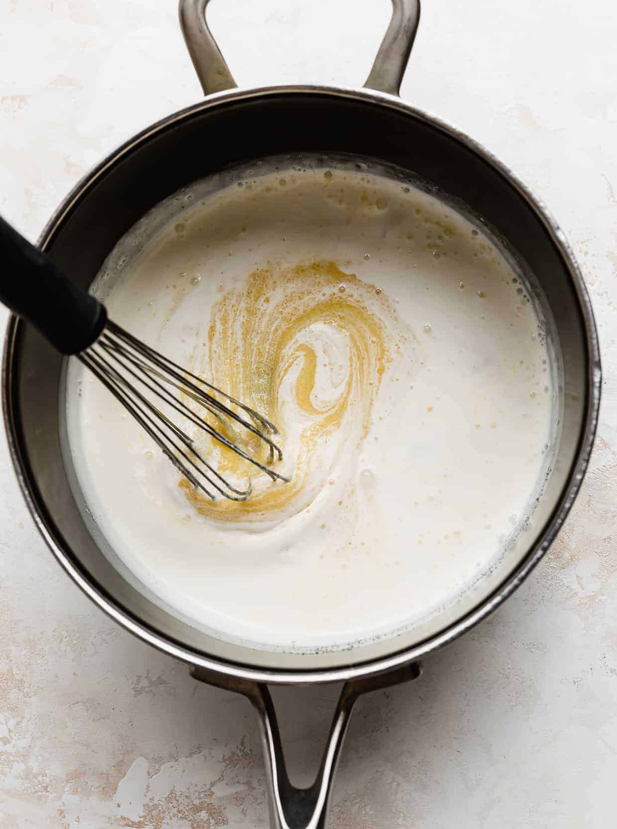 A whisk stirring the heavy cream, sugar, and egg yolks in a saucepan. 