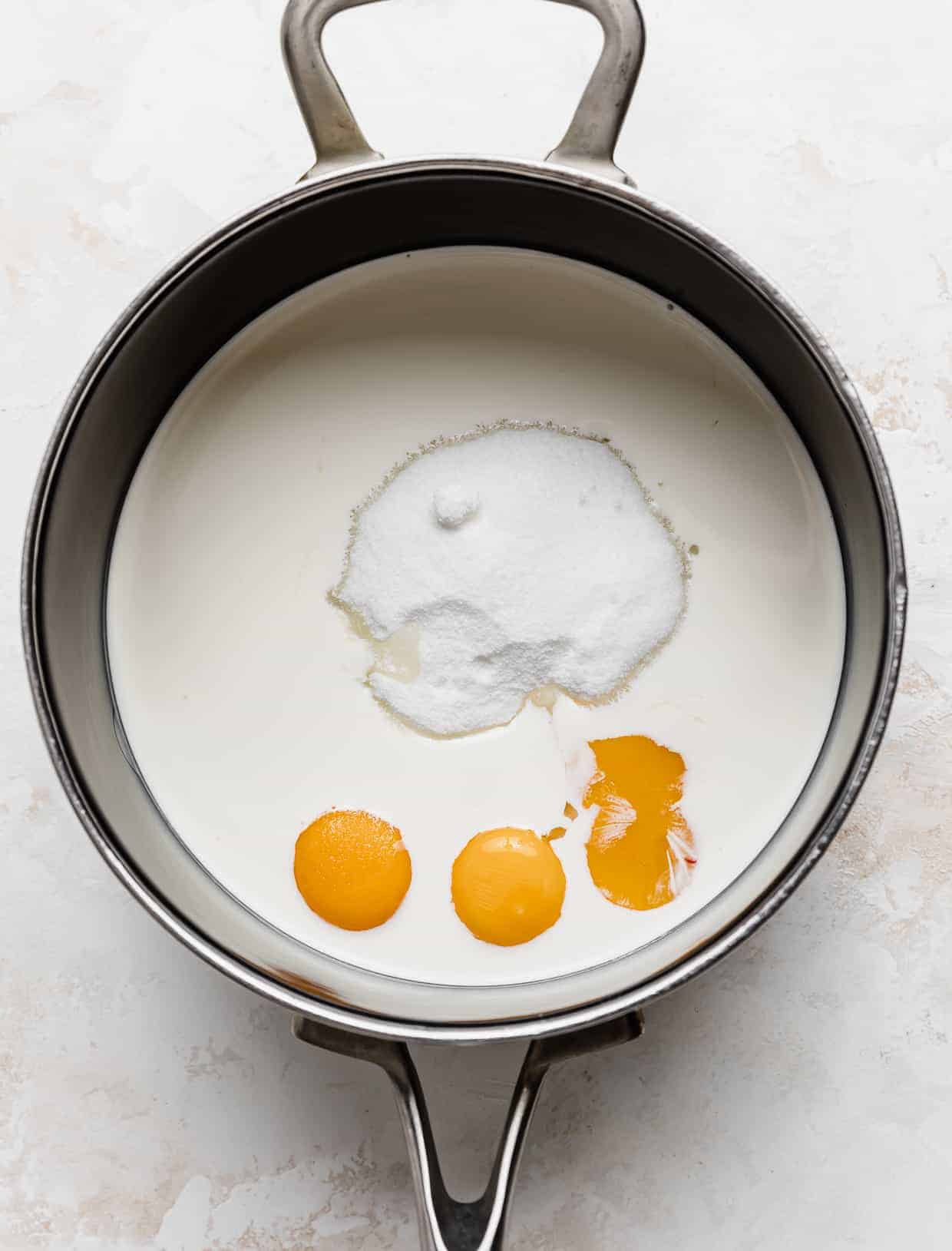 A black saucepan with heavy cream, sugar, and 3 egg yolks in it.