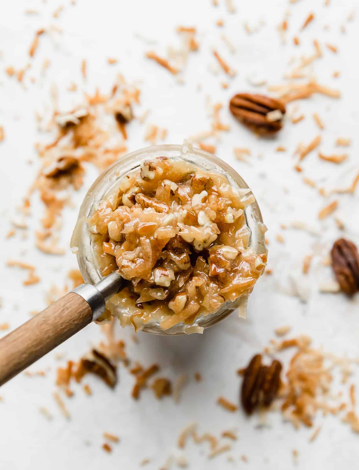 Overhead photo of German Chocolate Cake Frosting in a glass cup with toasted coconut and pecans around the perimeter of the cup.