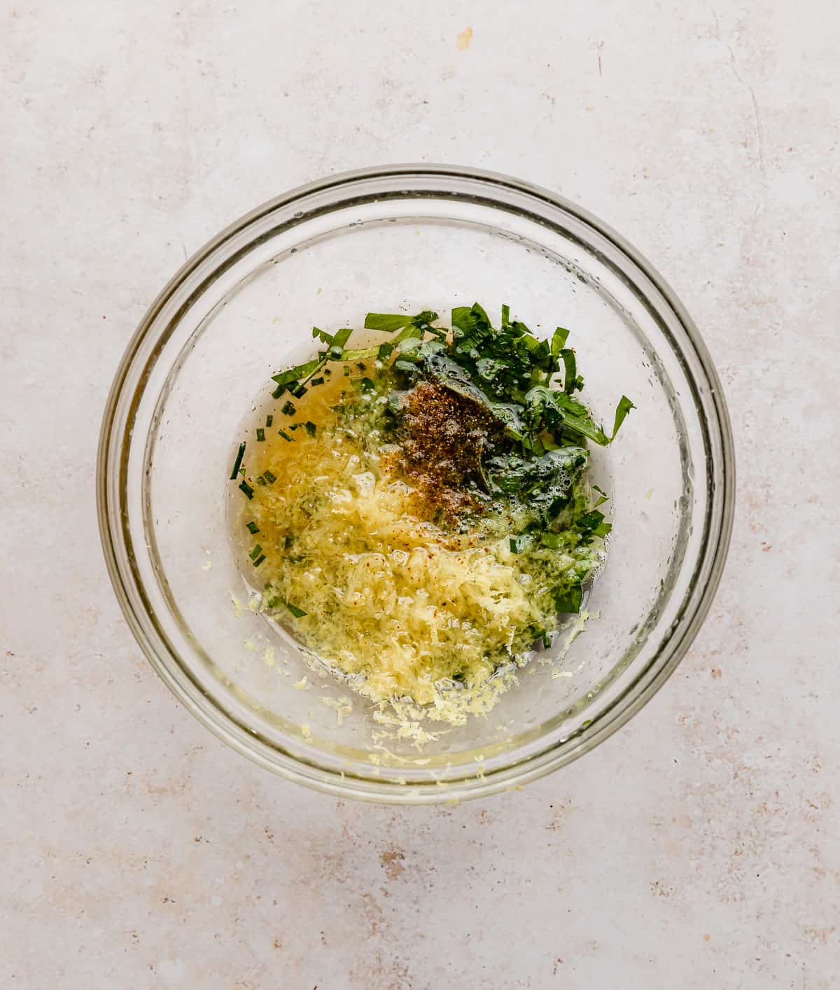 A glass bowl with chopped parsley, chives, honey, lemon, and lemon zest.