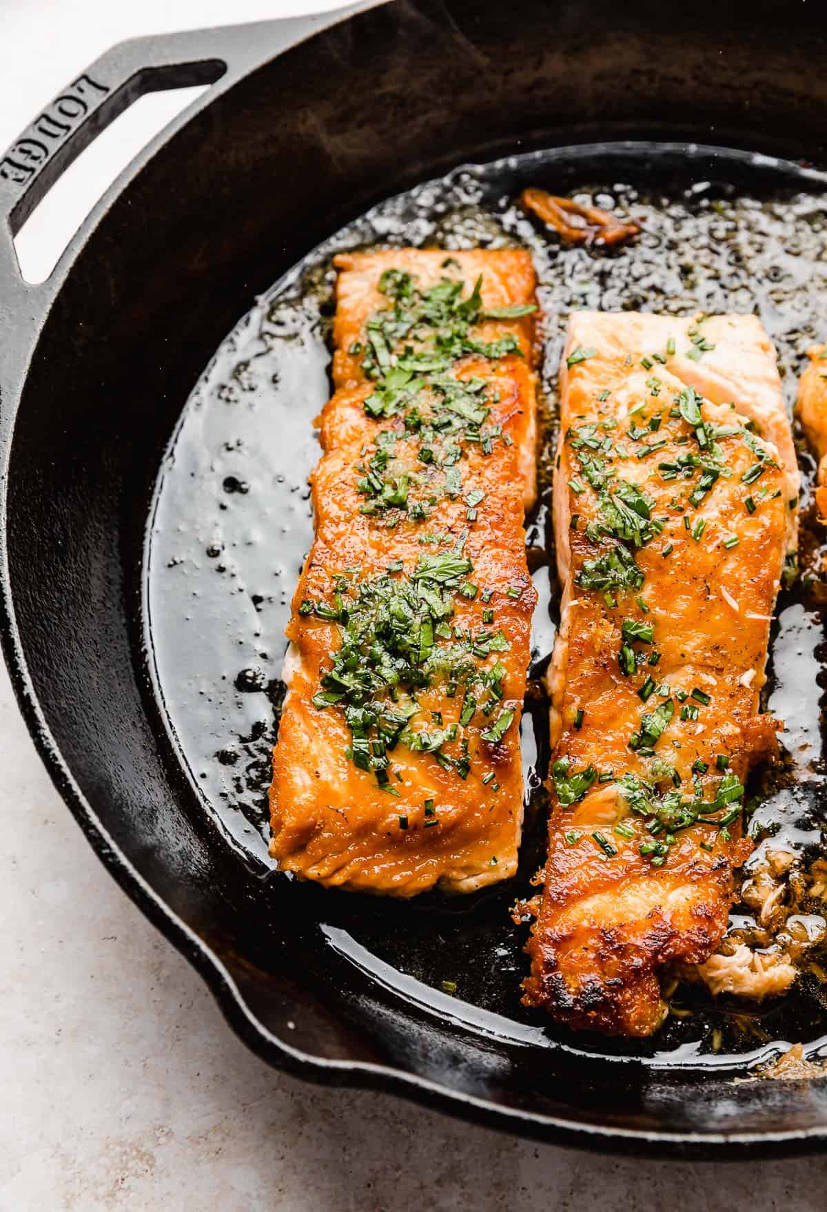 A lemon honey sauce with parsley and chives overtop cooked salmon in a black skillet.
