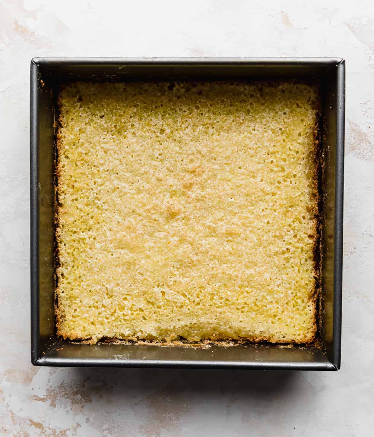 A square pan with baked yellow lemon bars in it, against a white and cream colored background.
