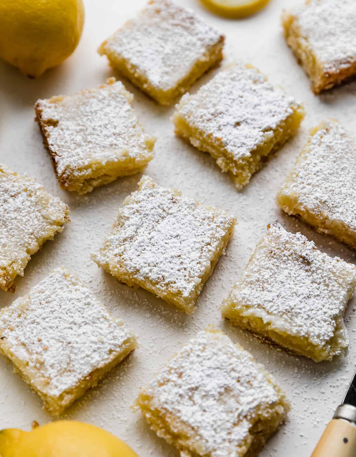 Lemon squares topped with powdered sugar and a glaze, on a white background.