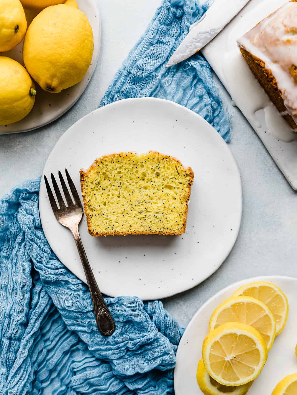 A slice of lemon poppy seed bread on a white plate with a fork next to the slice.