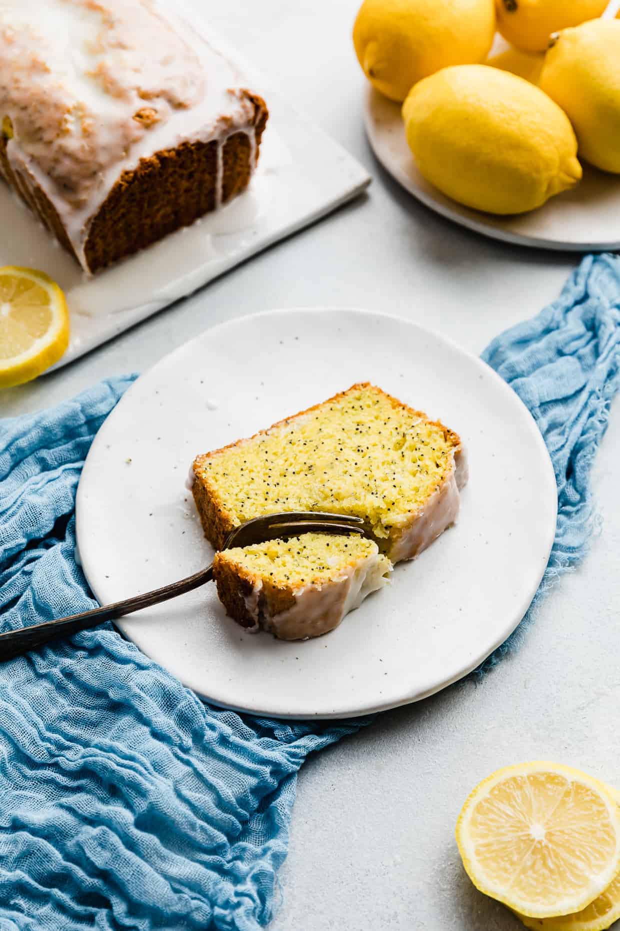 A fork cutting into a slice of lemon poppy seed bread on a white plate. 