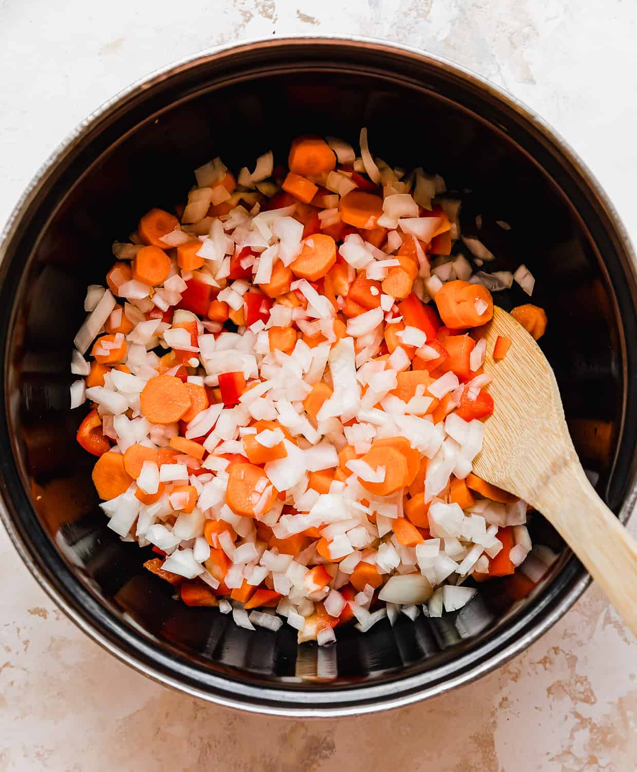 Black pot with chopped onion, red pepper, and carrots in it.