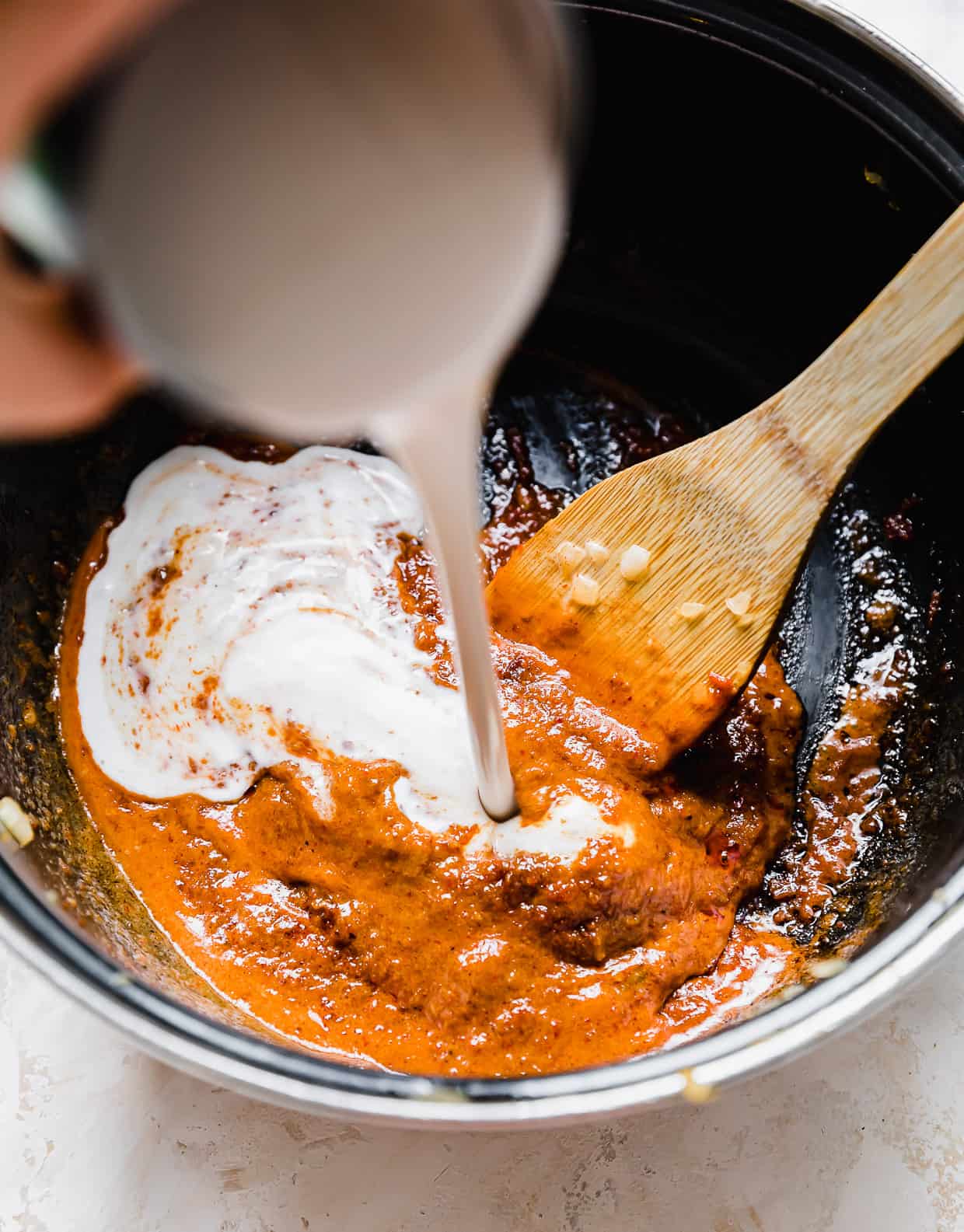 Coconut milk being poured into a pot with Massaman Curry paste at the bottom.