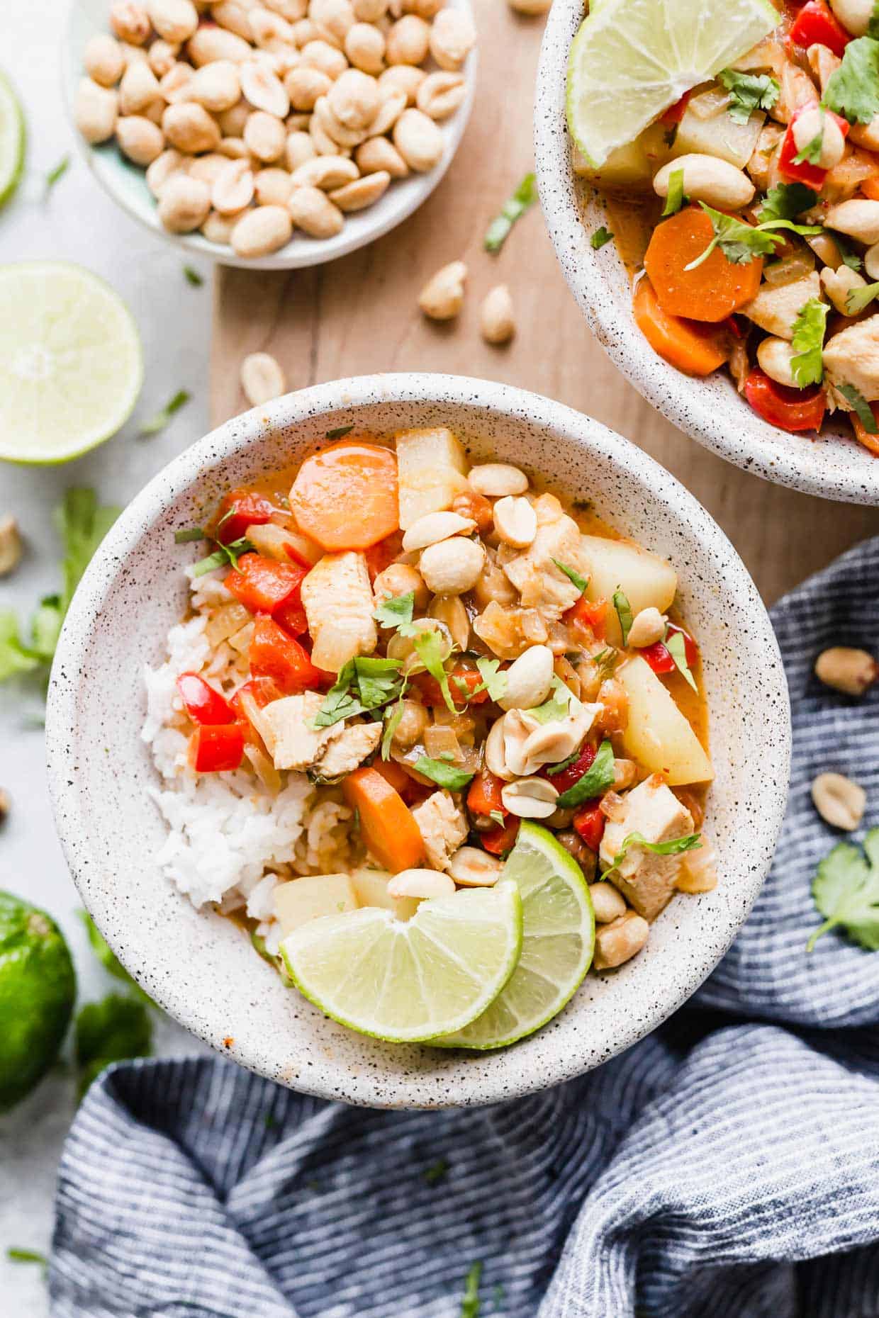 A bowl with Massaman Curry topped with limes, peanuts, and cilantro.