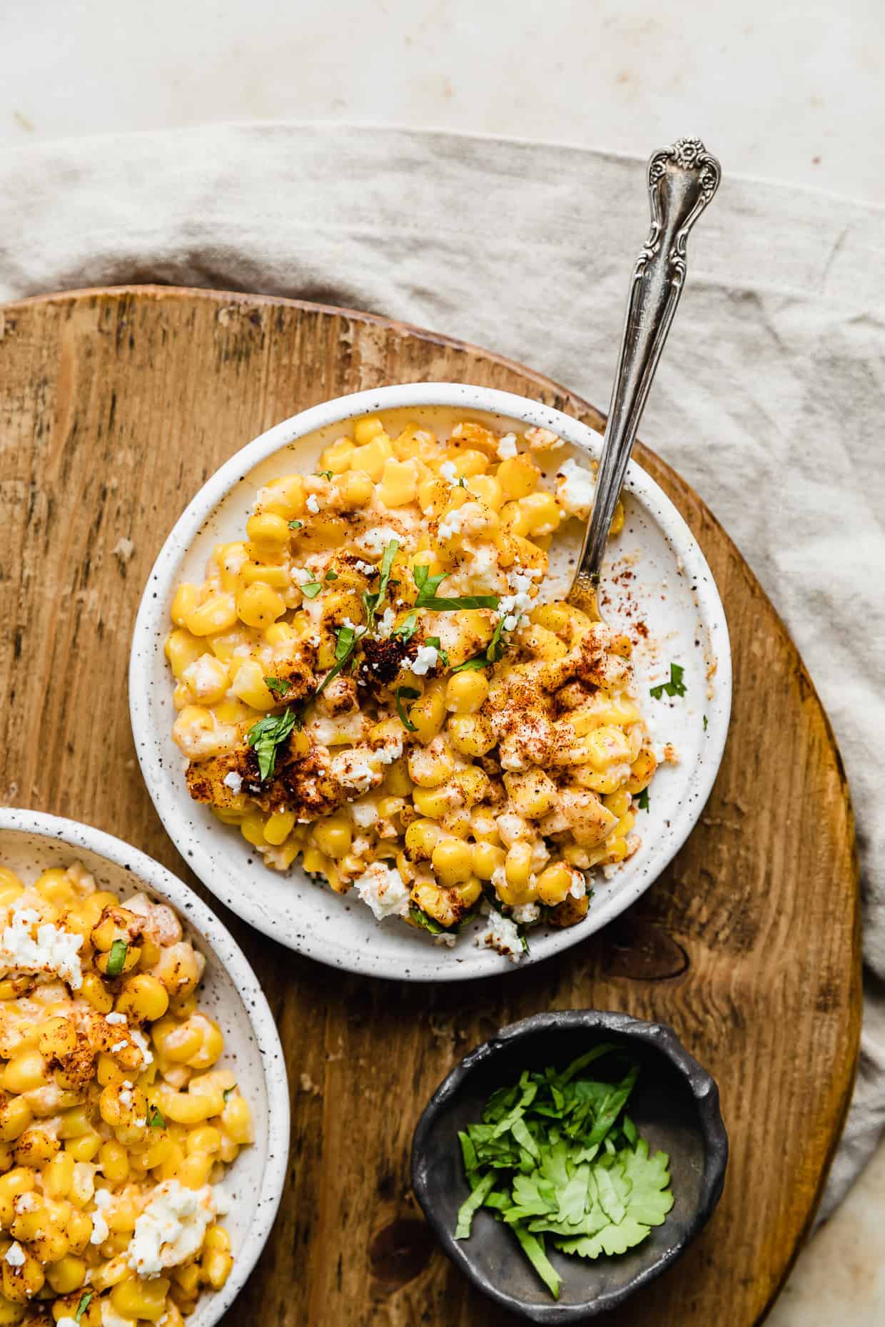 A white bowl with Mexican Street Corn Casserole in it, resting on a round wooden board. 