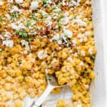A large serving spoon scooping out Mexican Street Corn Casserole from a white baking dish.
