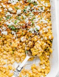 A large serving spoon scooping out Mexican Street Corn Casserole from a white baking dish.