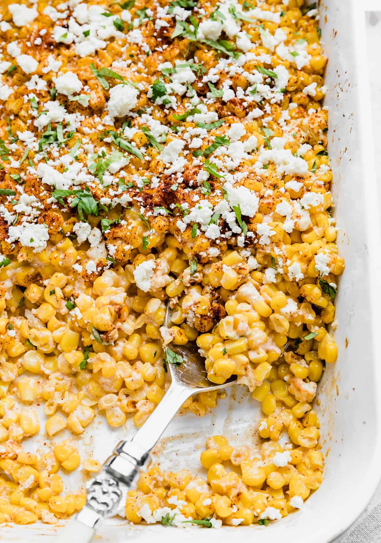 A large serving spoon scooping out Mexican Street Corn Casserole from a white baking dish.