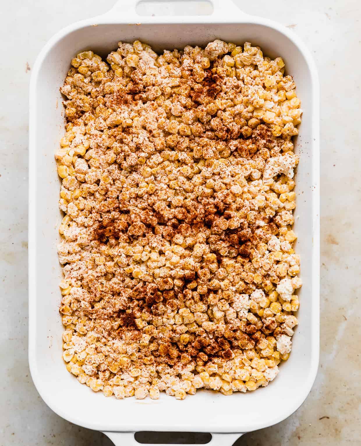 A white rectangular baking dish full of Mexican Street Corn Casserole that has been sprinkled with chili powder.
