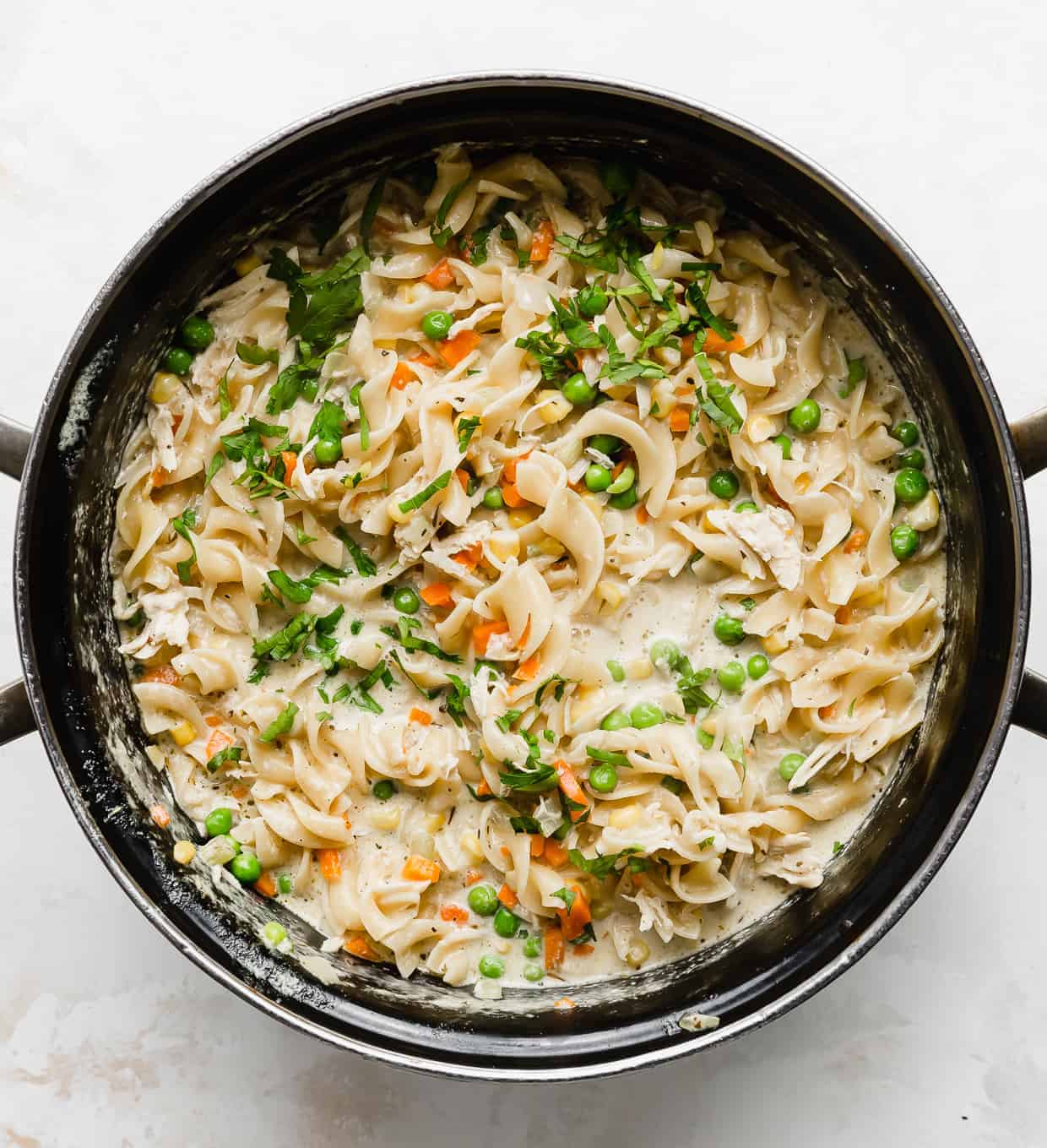 A pot full of egg noodles, diced carrots, and peas. 