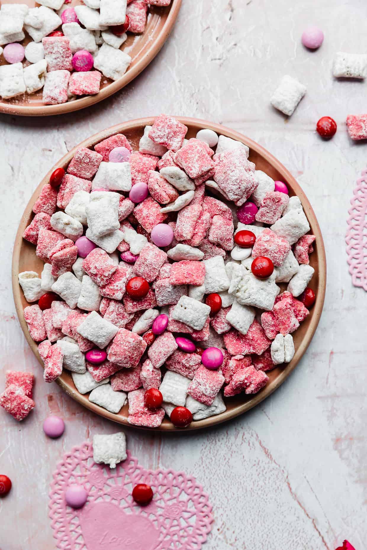 A plate of pink and white Valentine's Day Muddy Buddies against a gray background. 