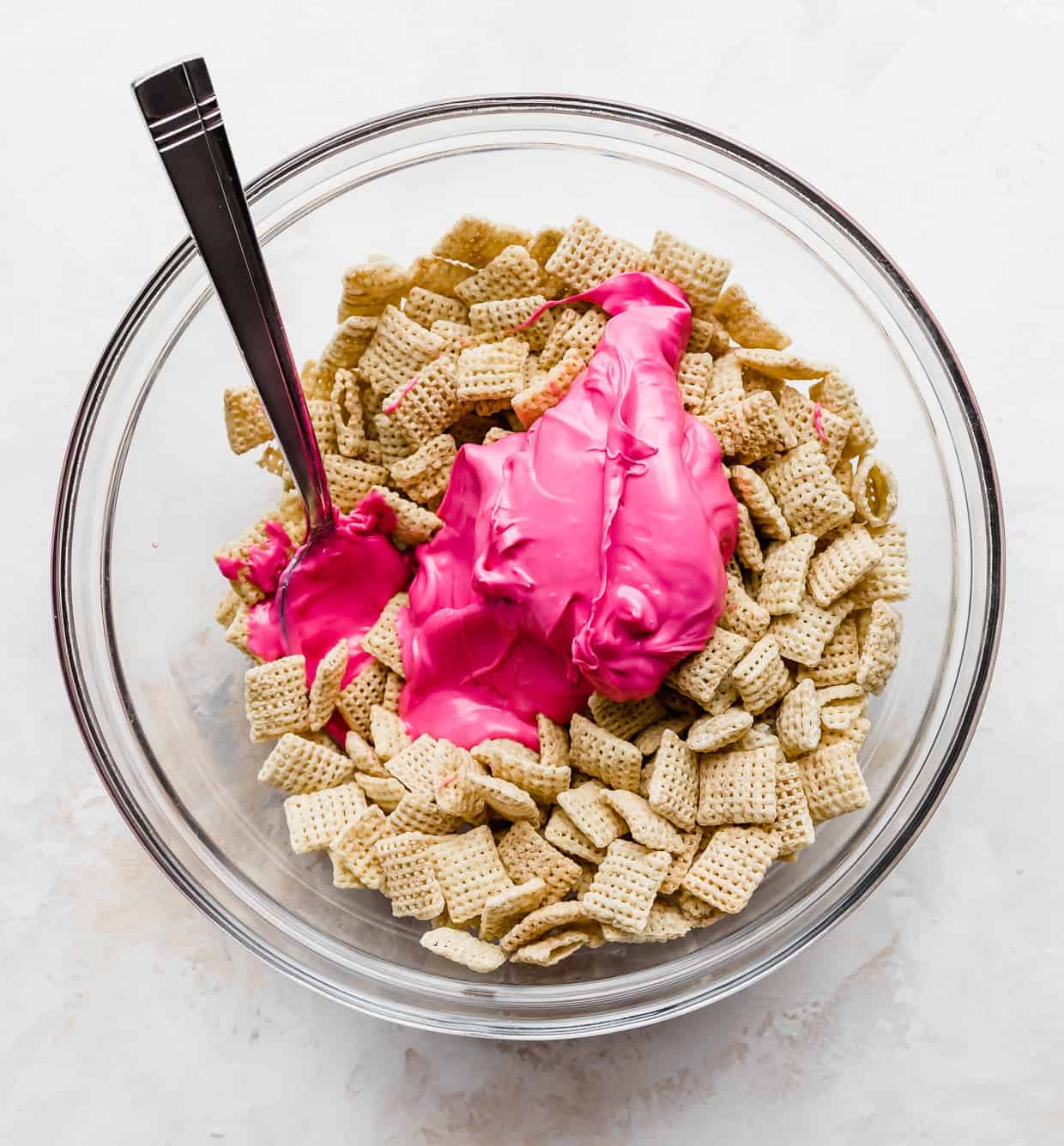 A glass bowl with Chex cereal and pink melted chocolate drizzled overtop.