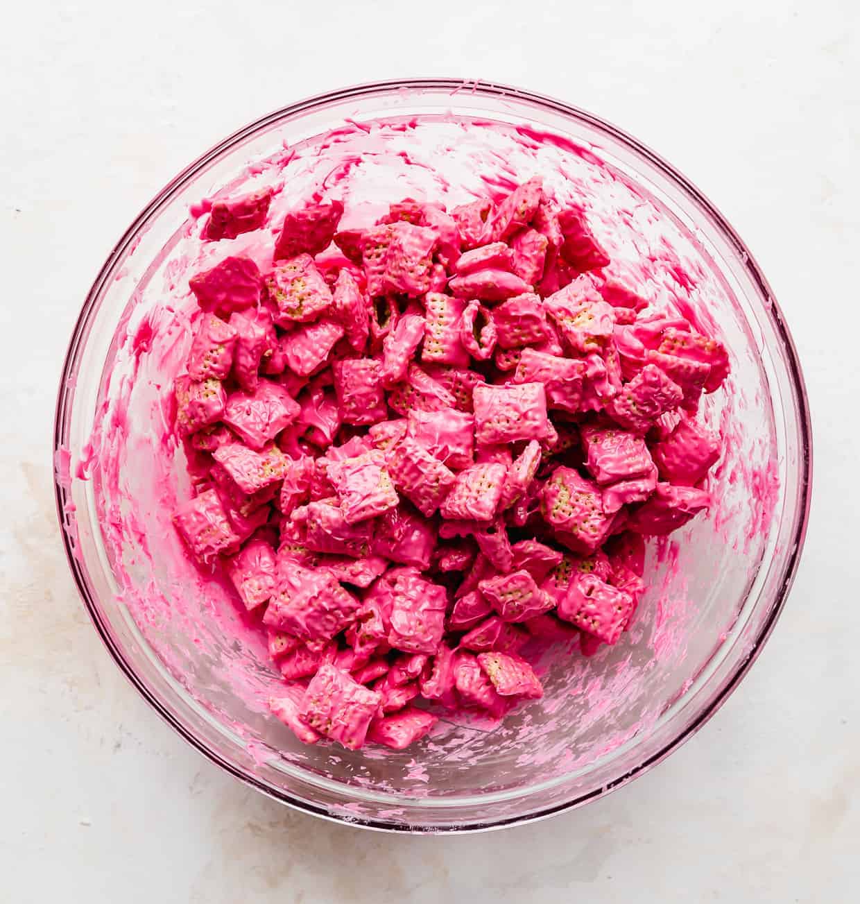 Bright pink covered Chex cereal in a glass bowl.