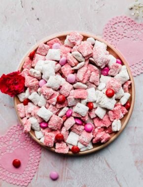 A plate of white and pink colored muddy buddies tossed with pink, red, and white M&M candy.