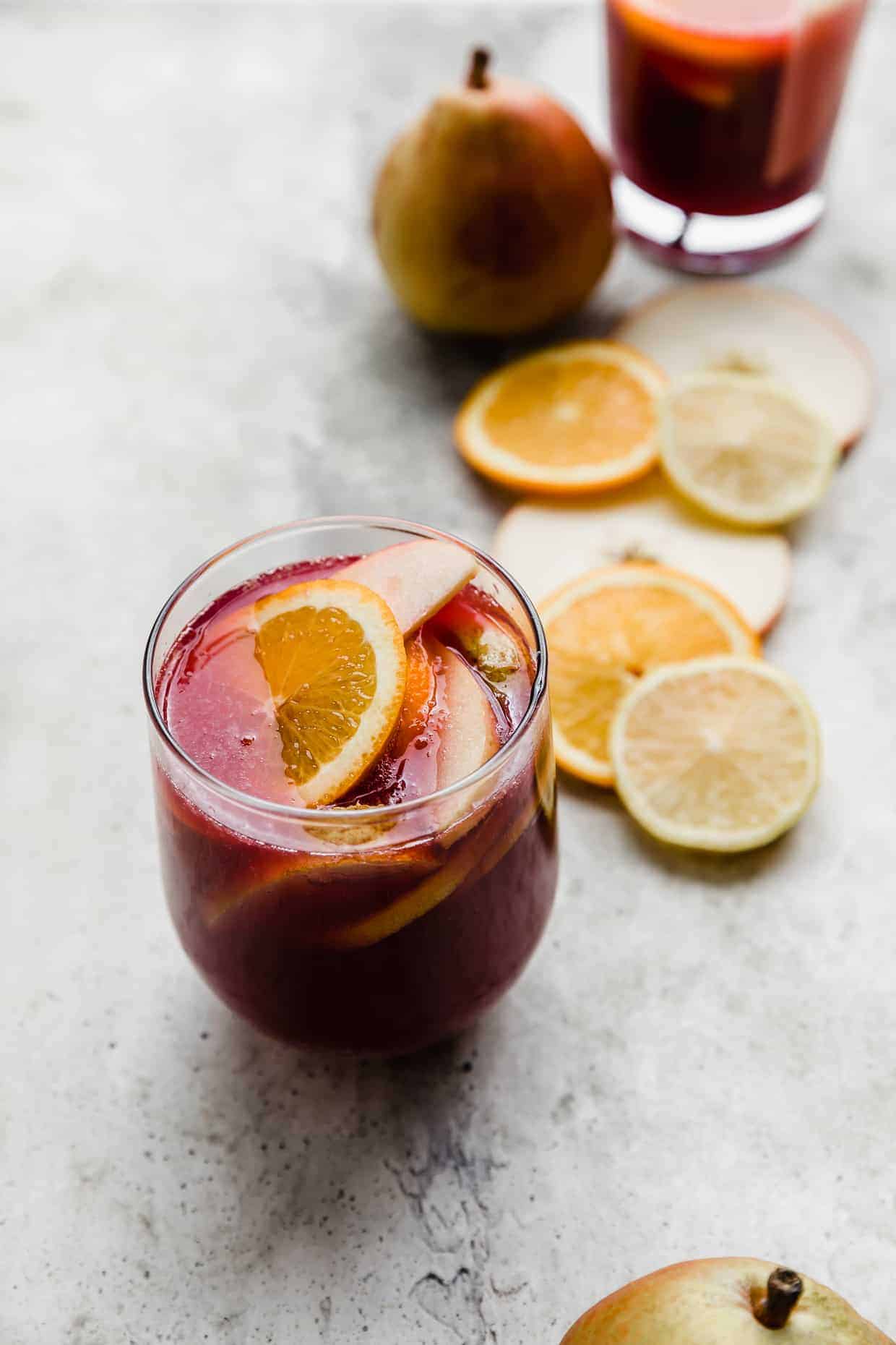 Purple colored sangria with slices of oranges, lemons, and pears floating in the cup. 