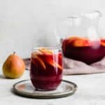 A glass of dark purple colored virgin sangria sitting on a gray plate.