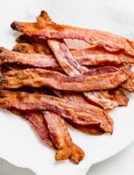 Crispy cooked bacon on a white paper towel covered plate.