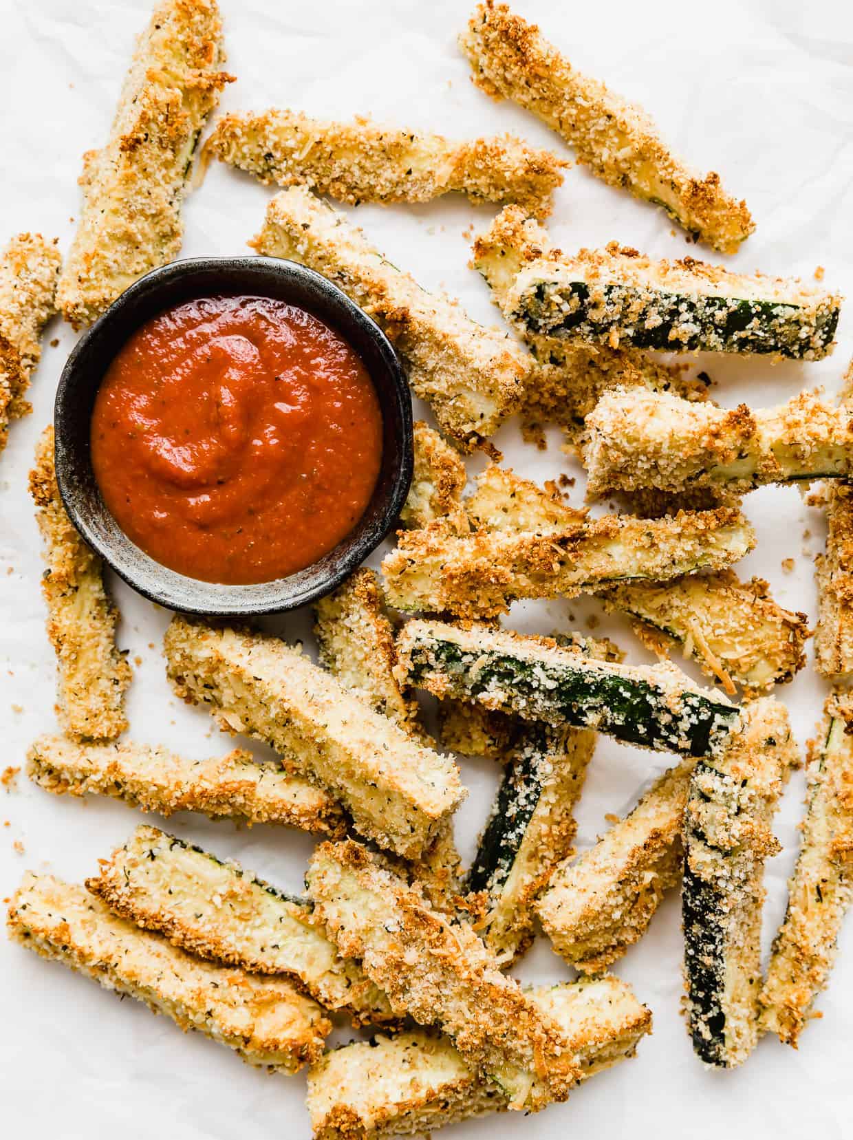 Zucchini fries on a white background with a small bowl of marinara sauce next to the fries.