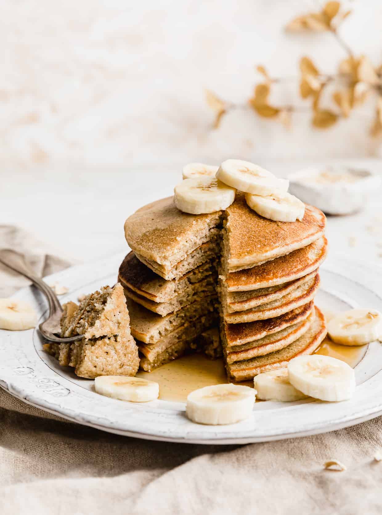 A stack of banana oatmeal pancakes with a wedge of pancakes cut from the stack. 