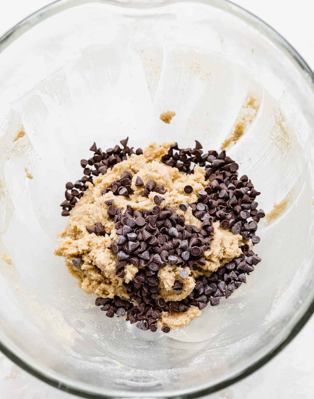 Mini chocolate chips added to a glass bowl with edible cookie dough in it.