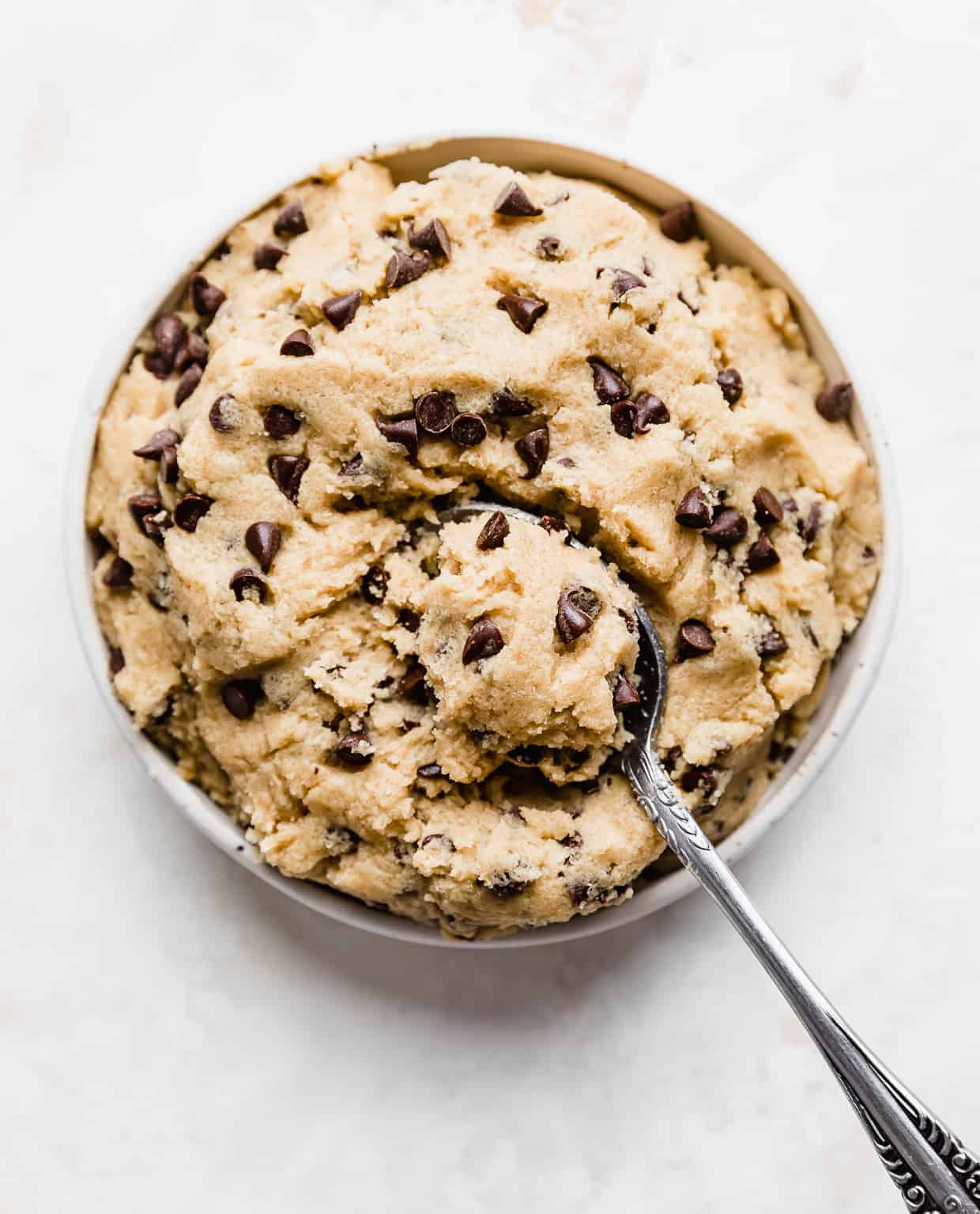 A plate full of chocolate chip cookie dough with a spoon scooping up a portion of the dough.