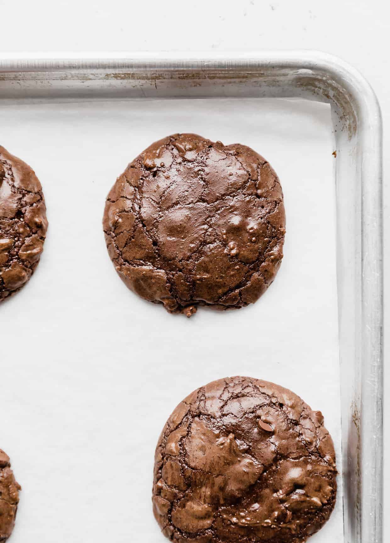A freshly baked Brownie mix cookie with a crackly top, on a parchment lined baking sheet against a white background.