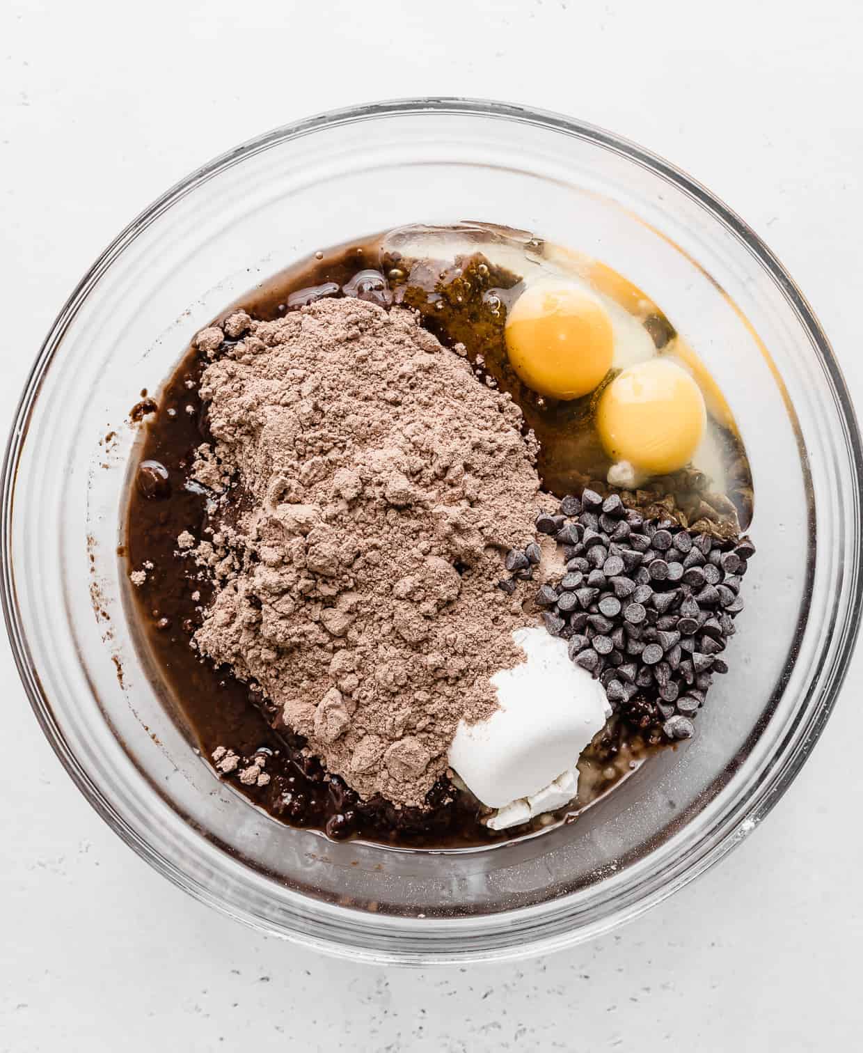 A glass bowl with dry brownie mix, 2 eggs, chocolate chips, and oil in it.