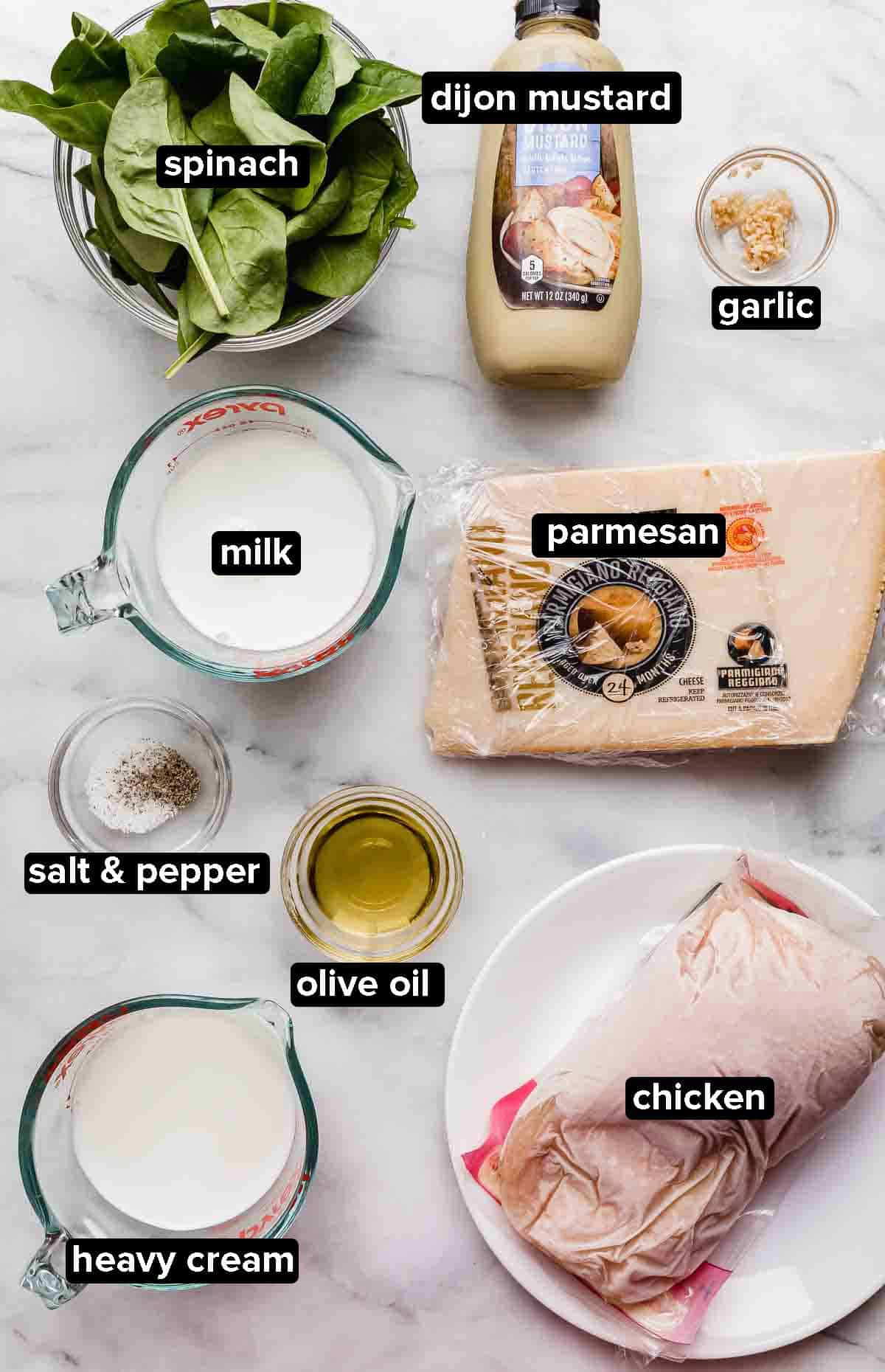 Chicken Dijon recipe ingredients on a white background: raw chicken breasts, parmesan, spinach, milk, heavy cream, dijon mustard, garlic, salt and pepper.