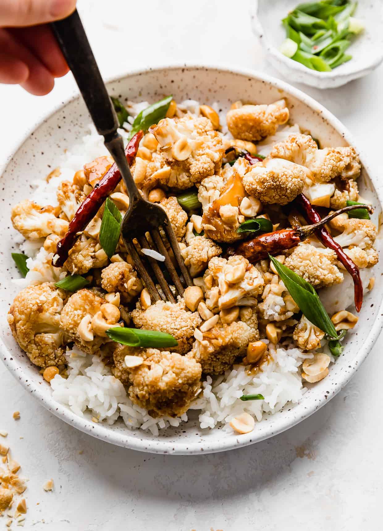 A fork piercing a roasted Kung Pao Cauliflower piece on a plate.