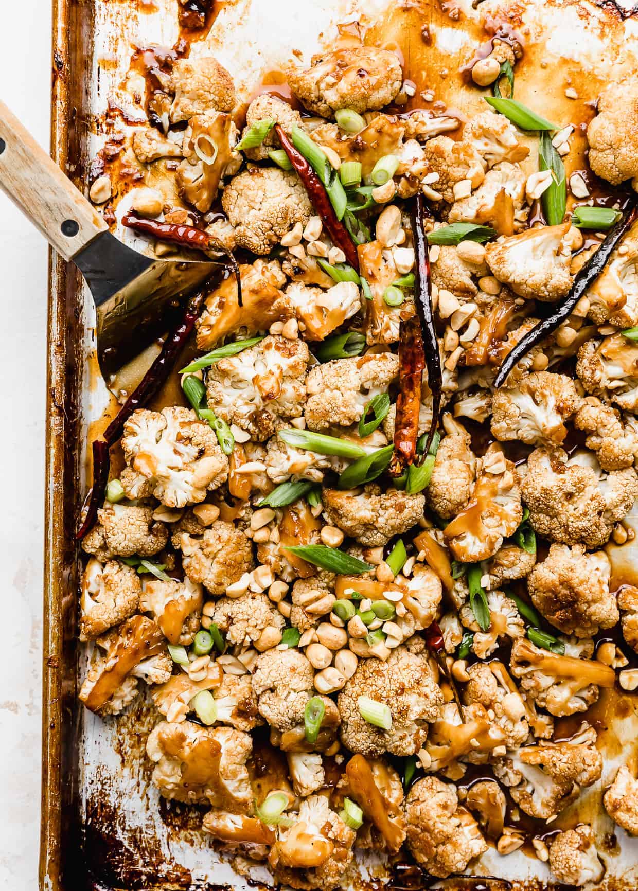 Kung Pao Cauliflower on a baking sheet with sliced green onions and peanuts overtop. 