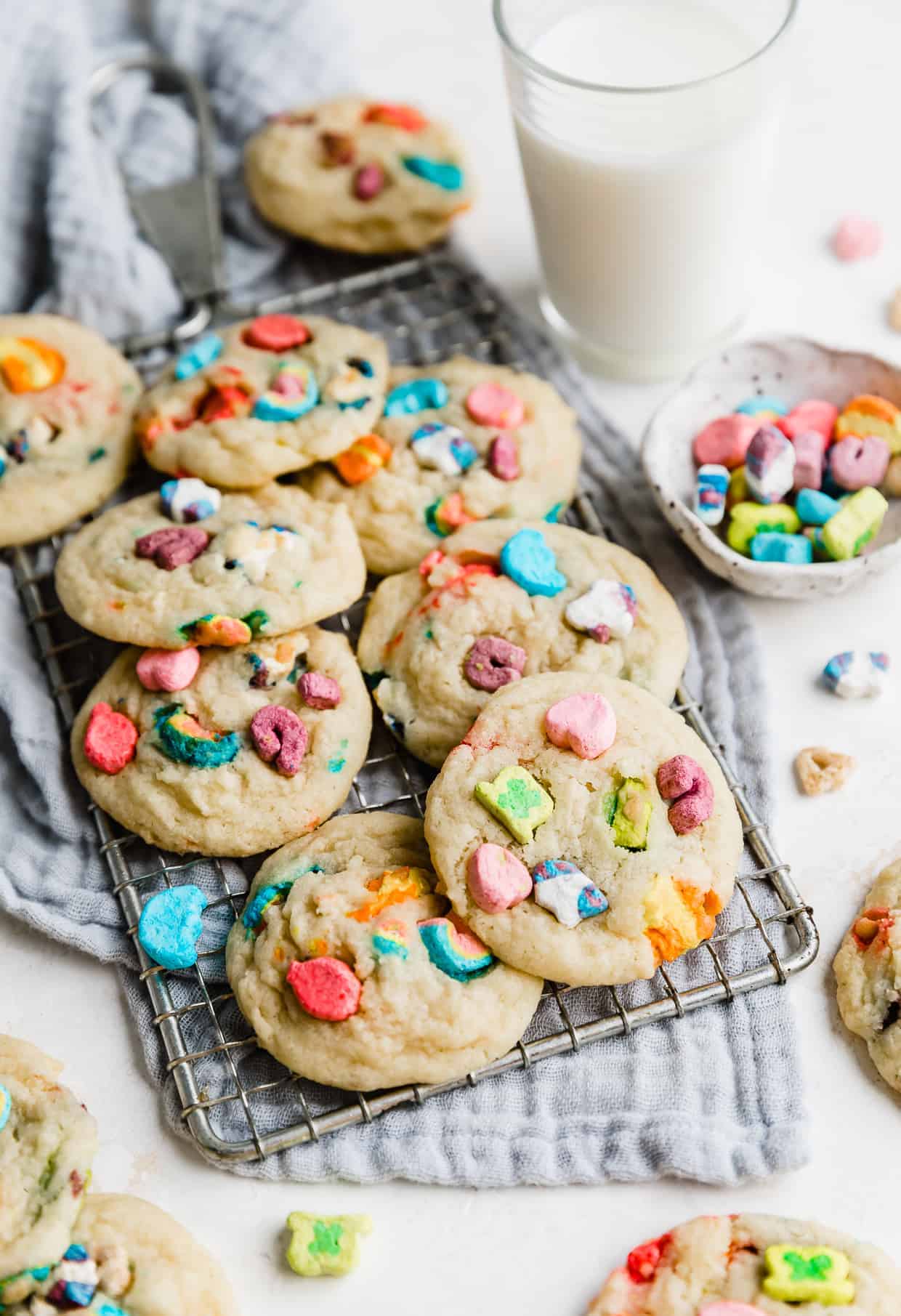 Several lucky charms marshmallow loaded sugar cookies on a wire rack against a gray napkin. 