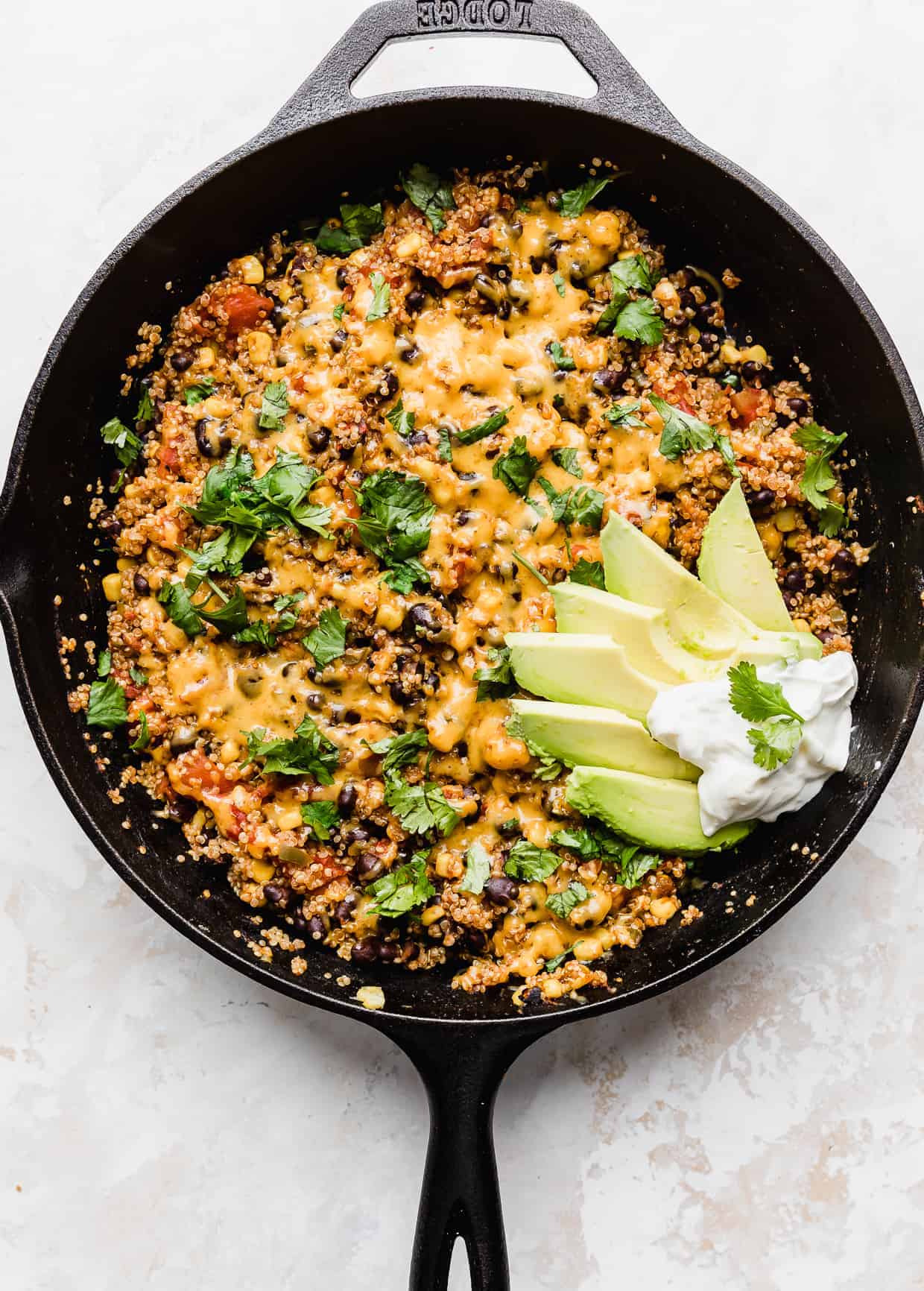 A skillet full of Mexican quinoa topped with cheese , cilantro, sliced avocados and sour cream. 