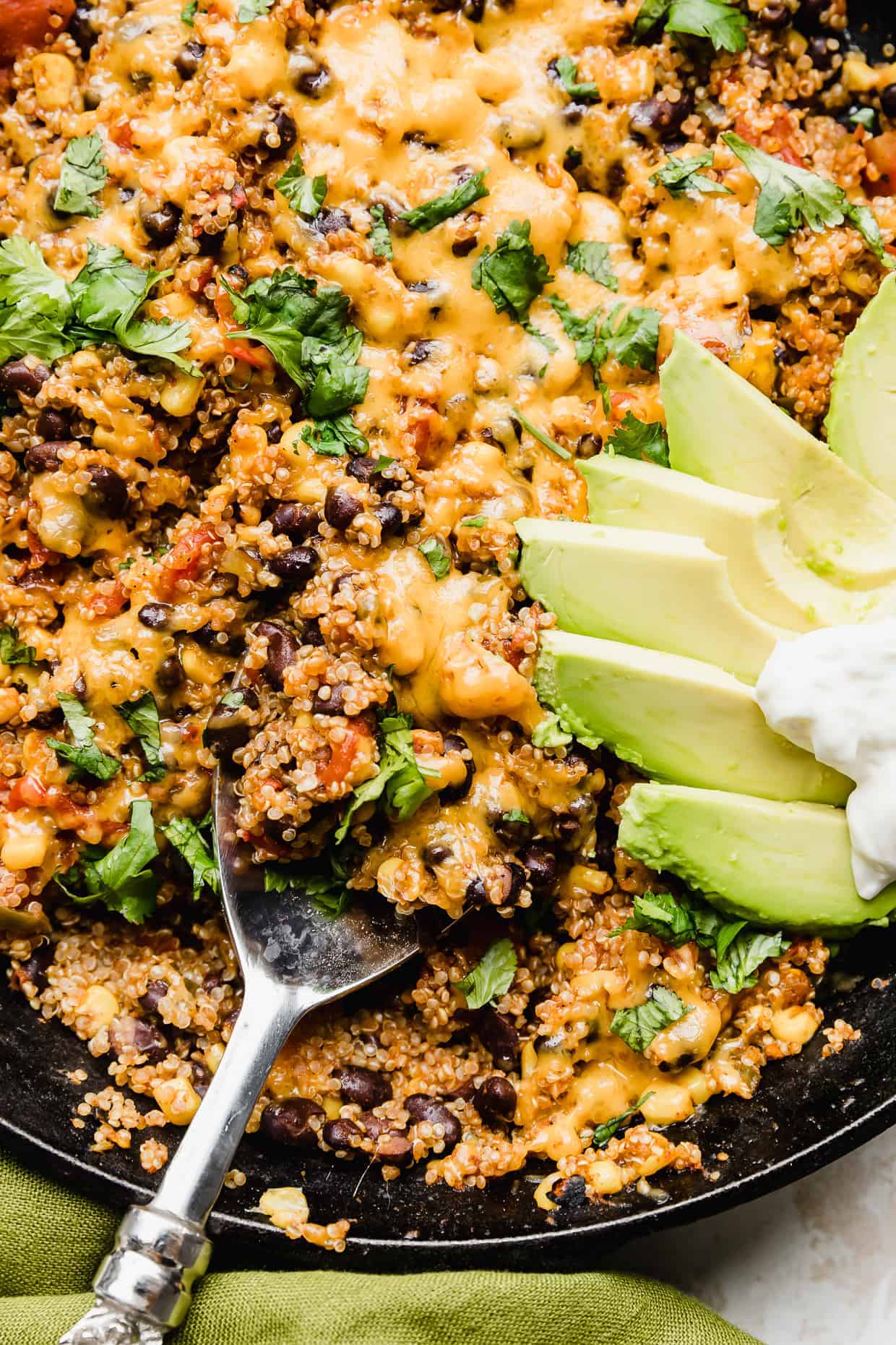 Close up photo of a serving spoon scooping up Mexican quinoa that is loaded with black beans, tomatoes, cheese, cilantro, and corn. 