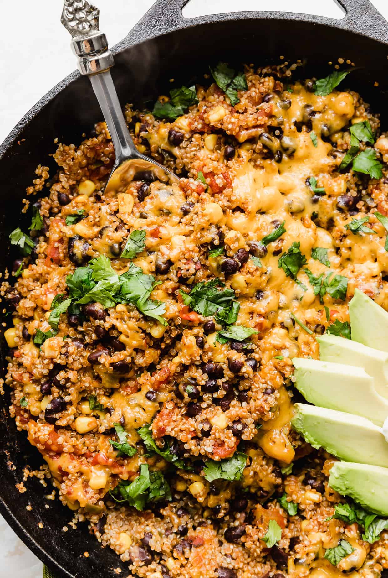 Mexican Quinoa in a black skillet topped with melted cheese and chopped cilantro. 